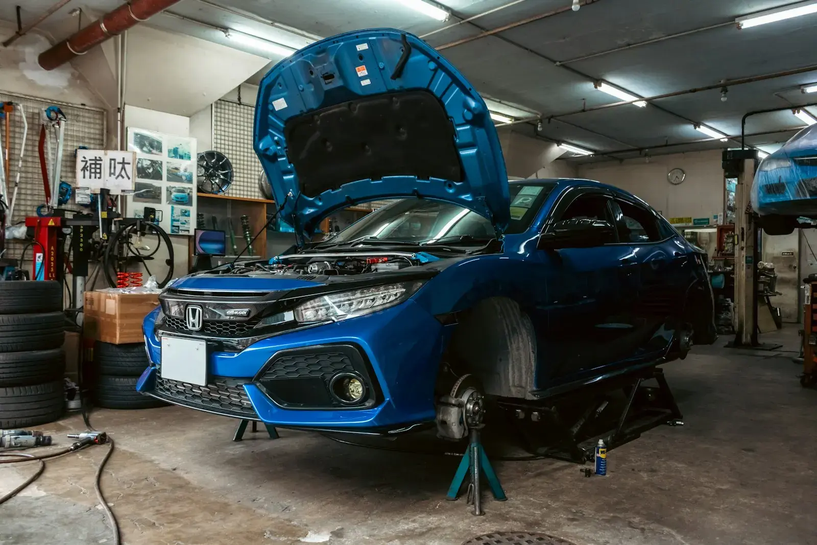 A blue honda civic with its hood open on a lift in a garage